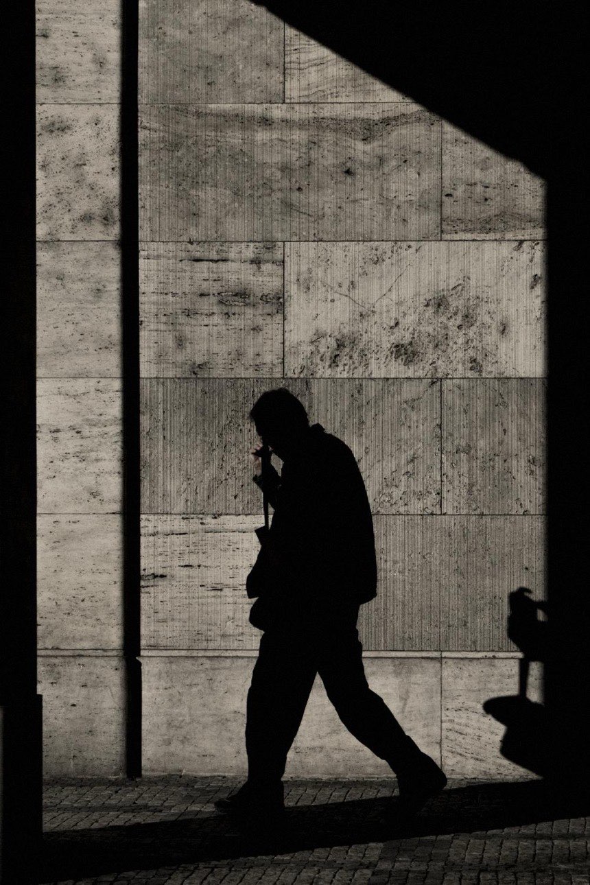 A man walking past a stone wall in hard sunlight, in silhouette. A message from Snags in Jira to Sara: launch on Friday or wait for the fix, two teams held up for 2 days.